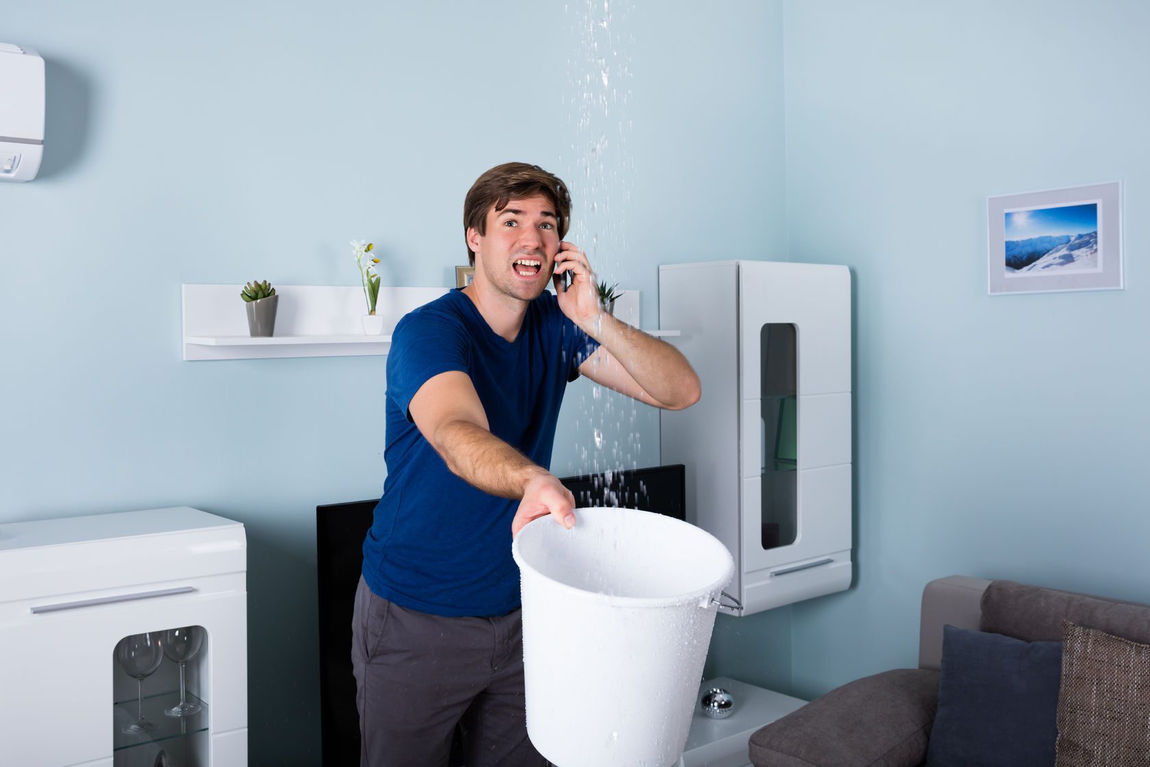 worried man calling plumber while leakage water falling into bucket at home